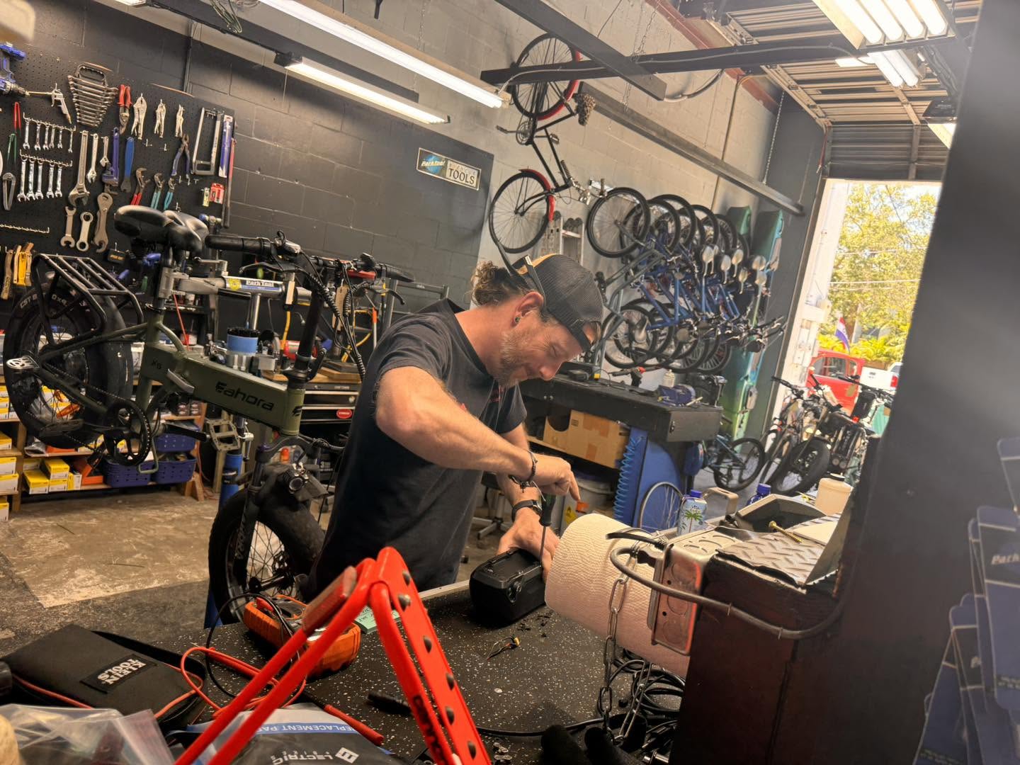 A mechanic works on an E-Bike battery at the bench in the Palm Harbor shop, bikes hanging on the wall behind him.
