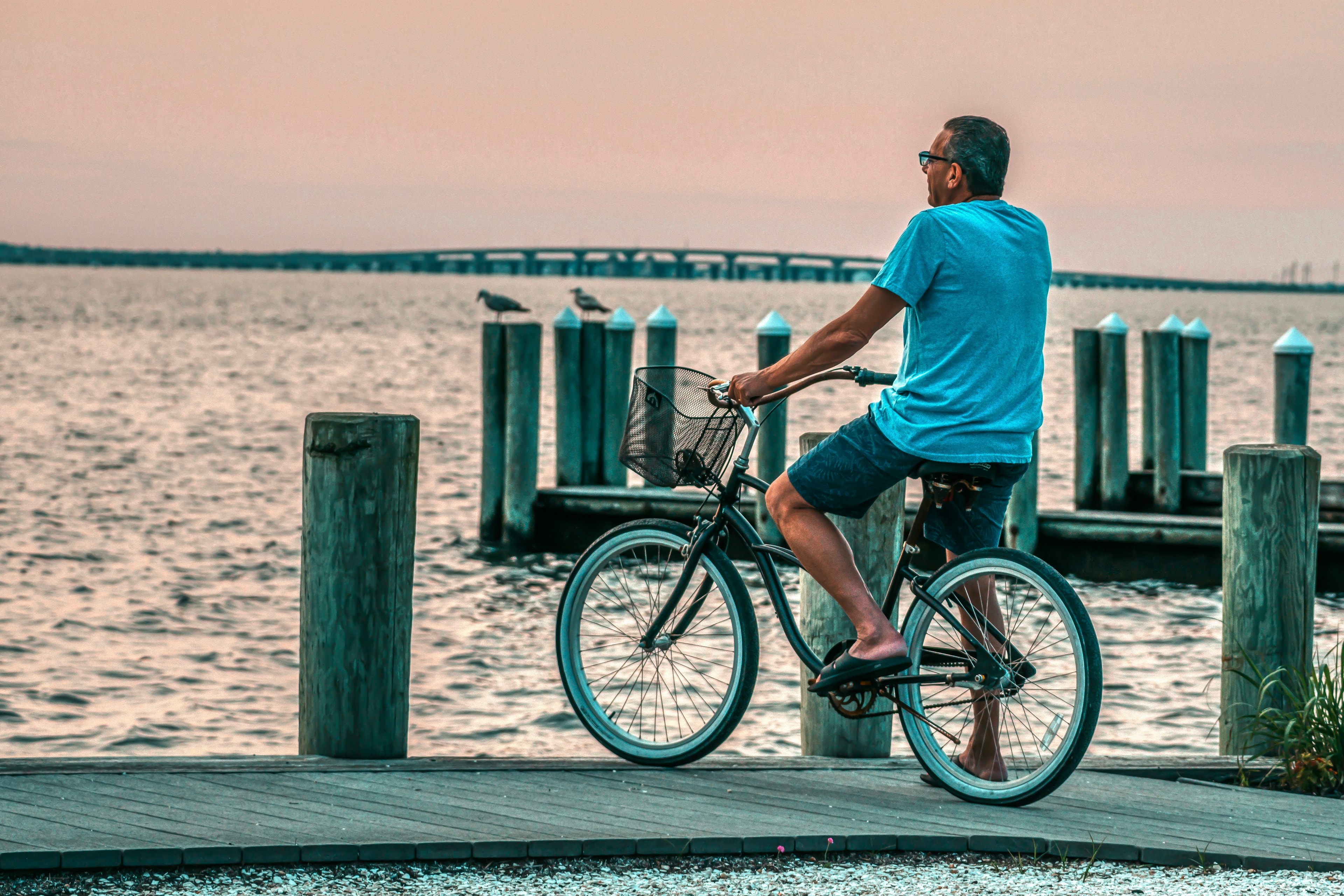 A rider on a cruiser pauses beside the pilings of a pier at dusk.