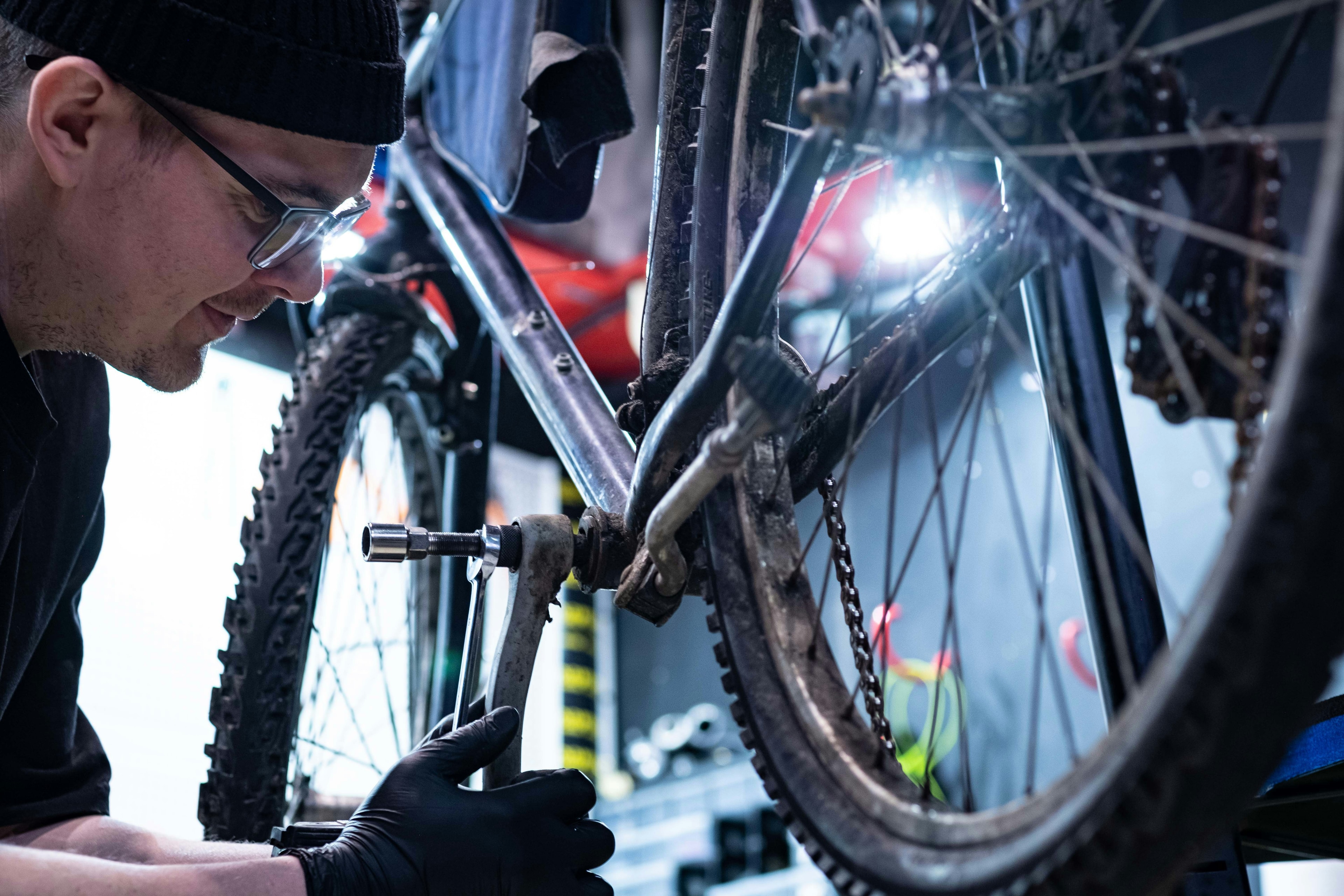A mechanic works on a mountain bike’s drivetrain under a bright work light.