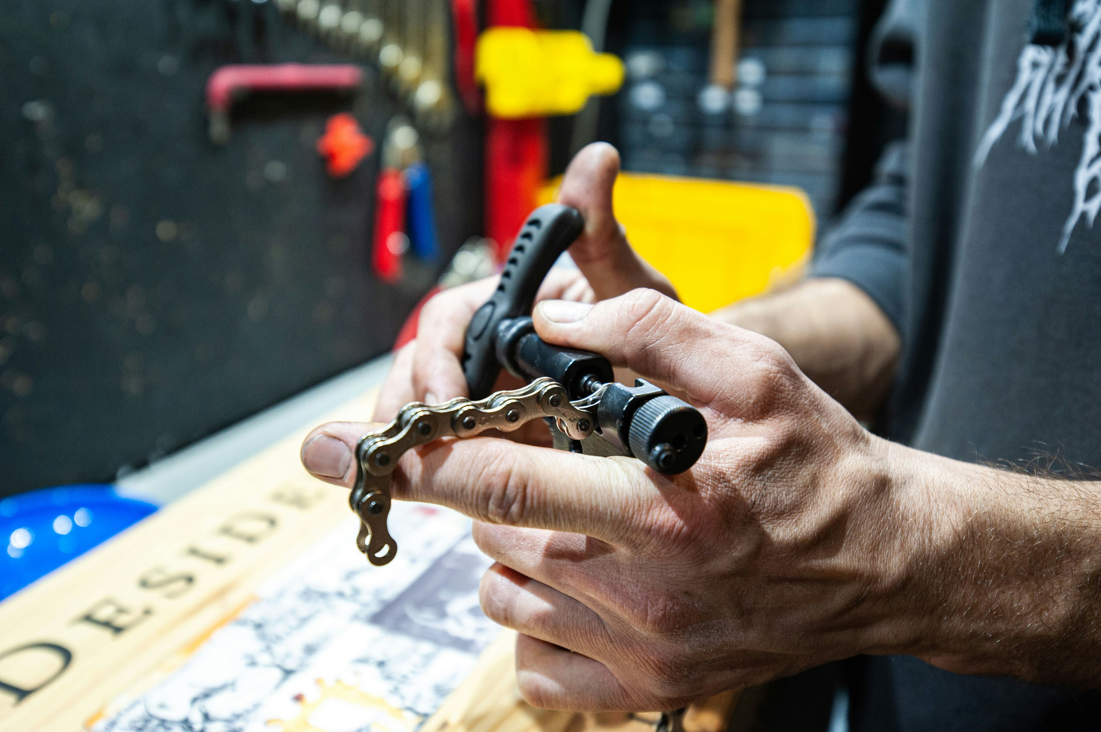 A mechanic’s hands work a chain tool on a bicycle chain.