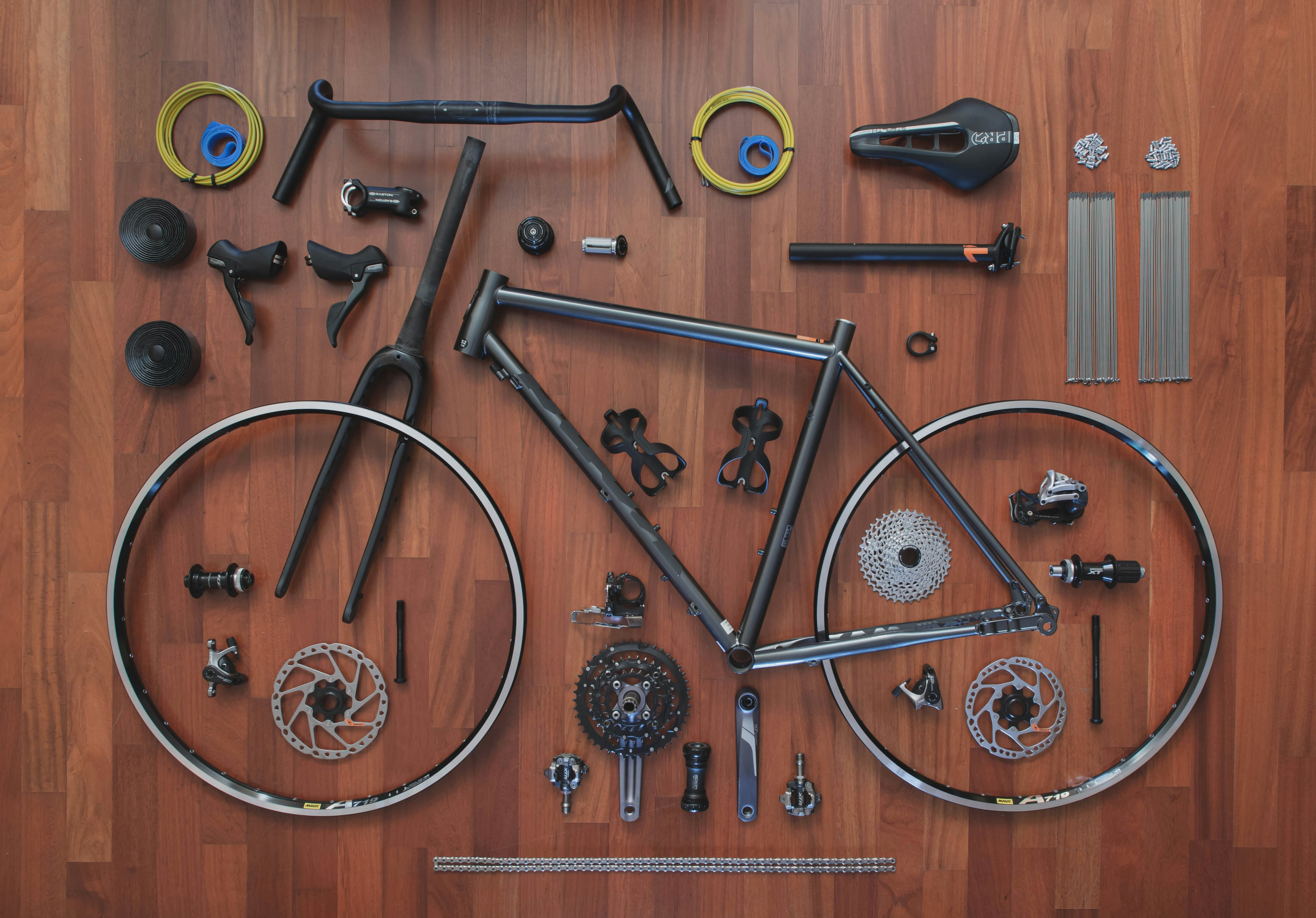 A bicycle fully disassembled and laid out part by part on a wooden bench.